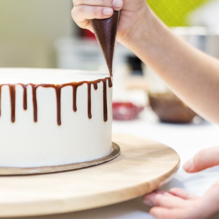 a person decorating a cake with liquid chocolate from a piping bag