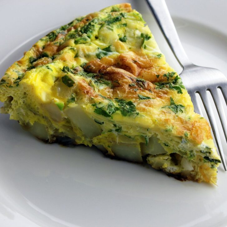slice of potato and kale frittata on a white plate with a fork