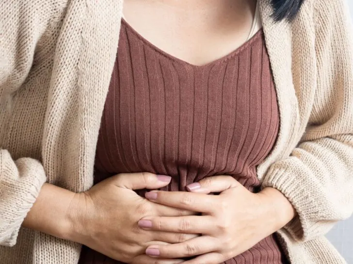 woman with a brown top and tan cardigan holding her stomach - signs of estrogen dominance