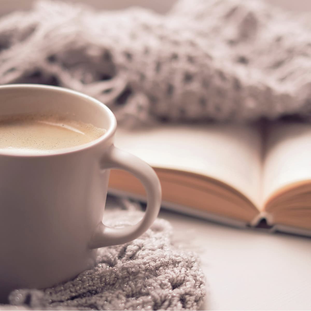 A cozy and serene moment of intentional living, featuring a warm cup of coffee resting on a soft, knitted blanket with an open book in the background. The soft lighting and simple setup evoke mindfulness, comfort, and the joy of slowing down to focus on meaningful moments.